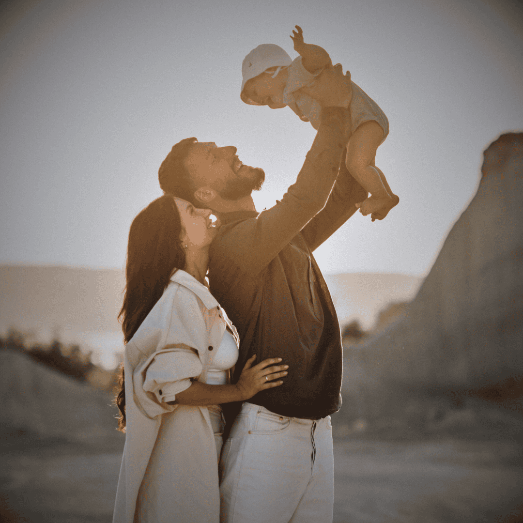 Junge Familie und Mann hält stolz sein kleines Baby nach oben, Frau umarmt ihn